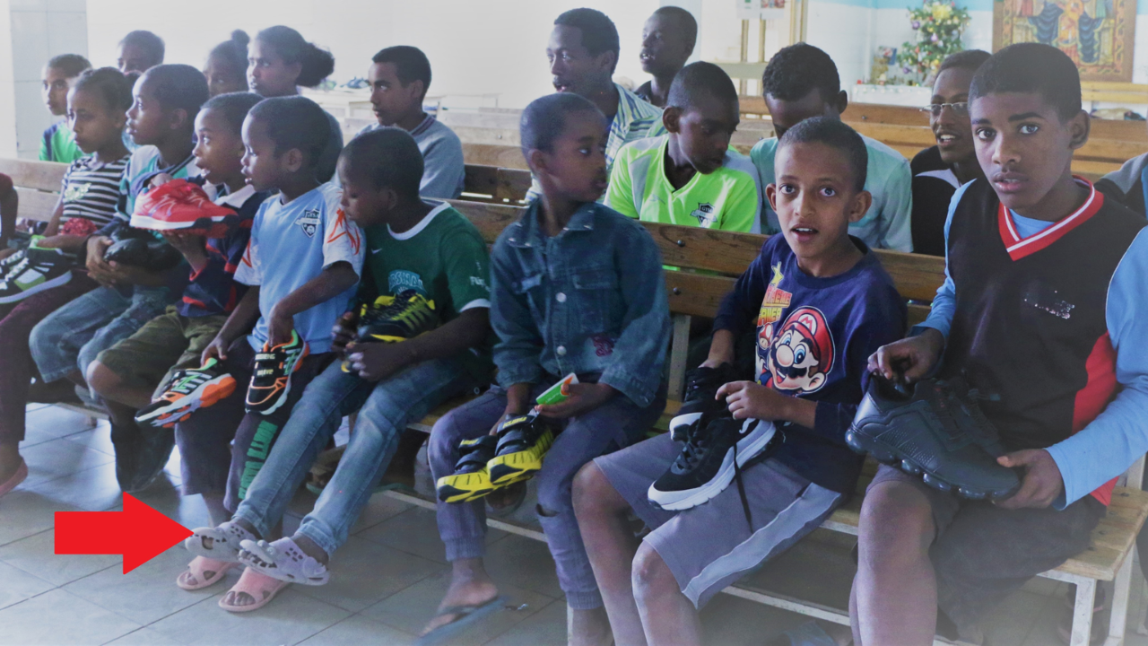 Children seated inside a church holding donated shoes during community outreach.