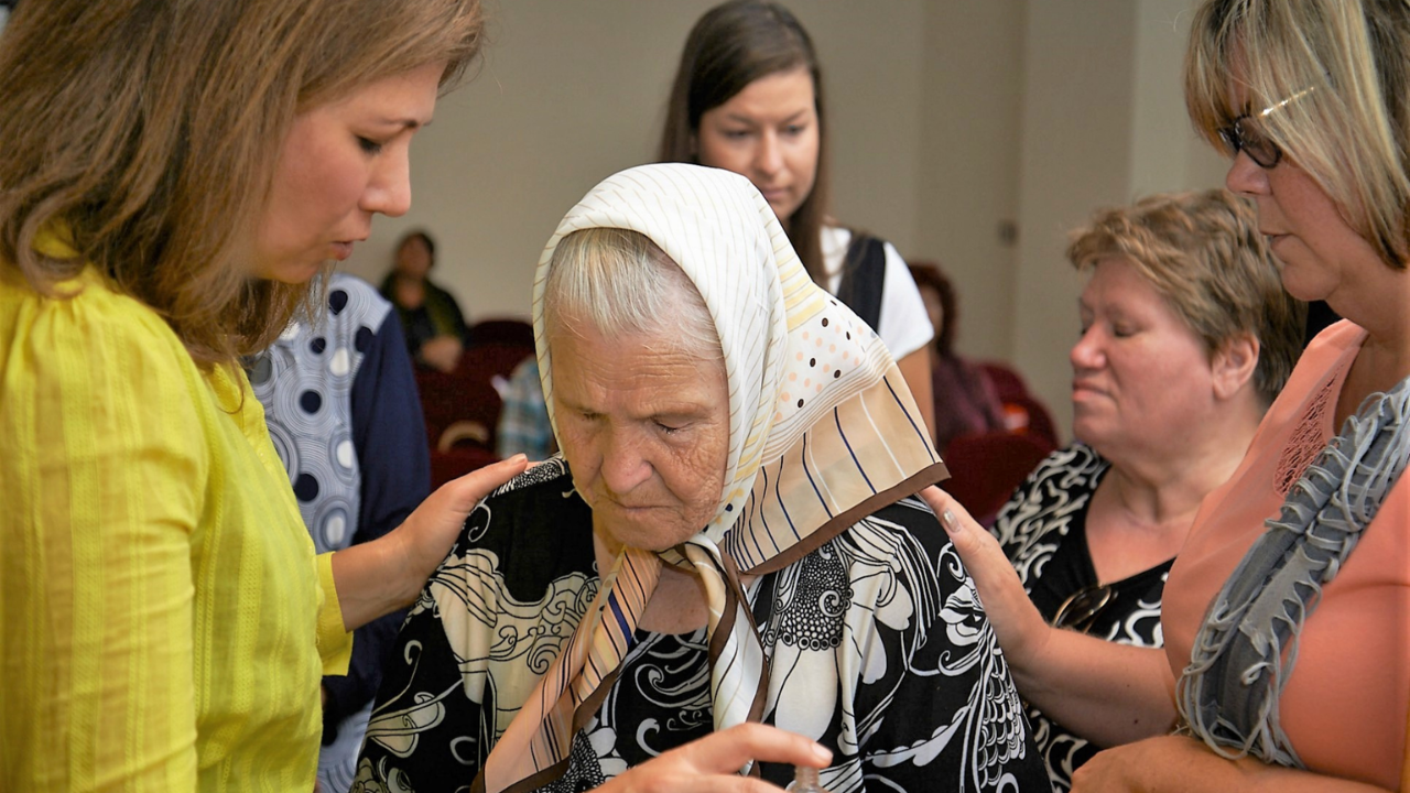 Mission volunteers praying with an elderly woman during community outreach.