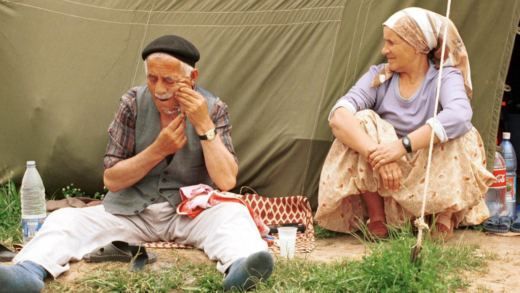 Elderly man taking medication while a woman sits beside him.
