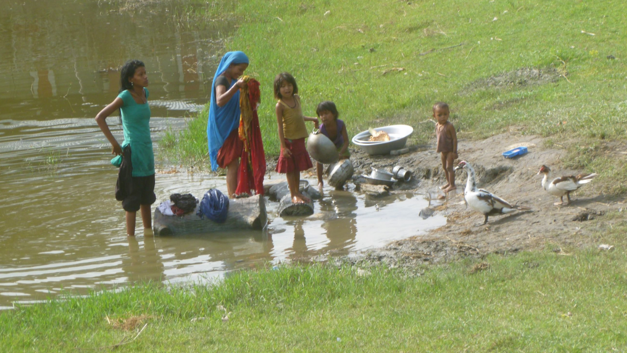 Women and children washing clothes beside a rural pond.