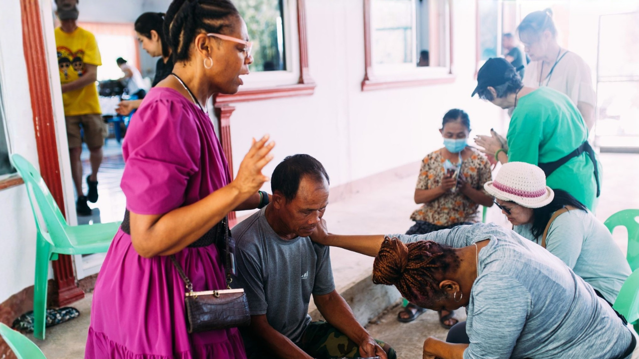 Christian mission team praying with community members after beginning their trip fundraising and payment plan.