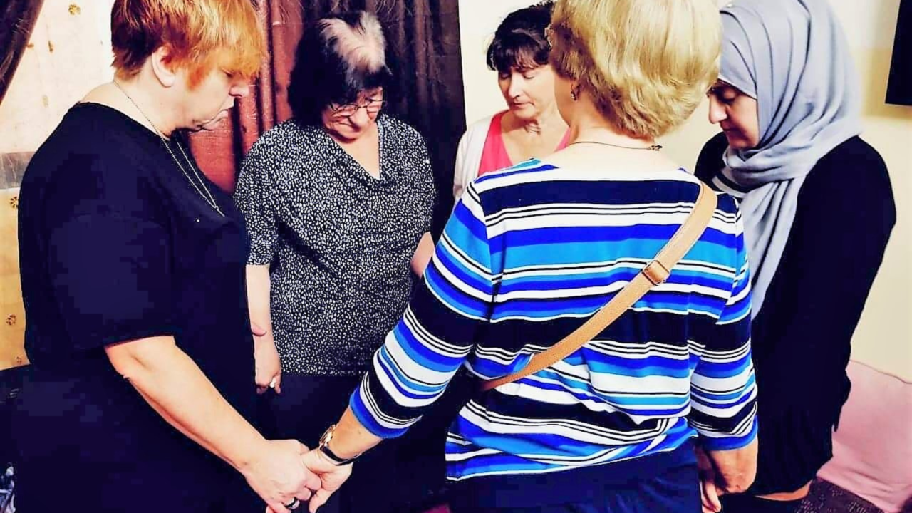 Diverse women holding hands and praying together during a mission gathering.